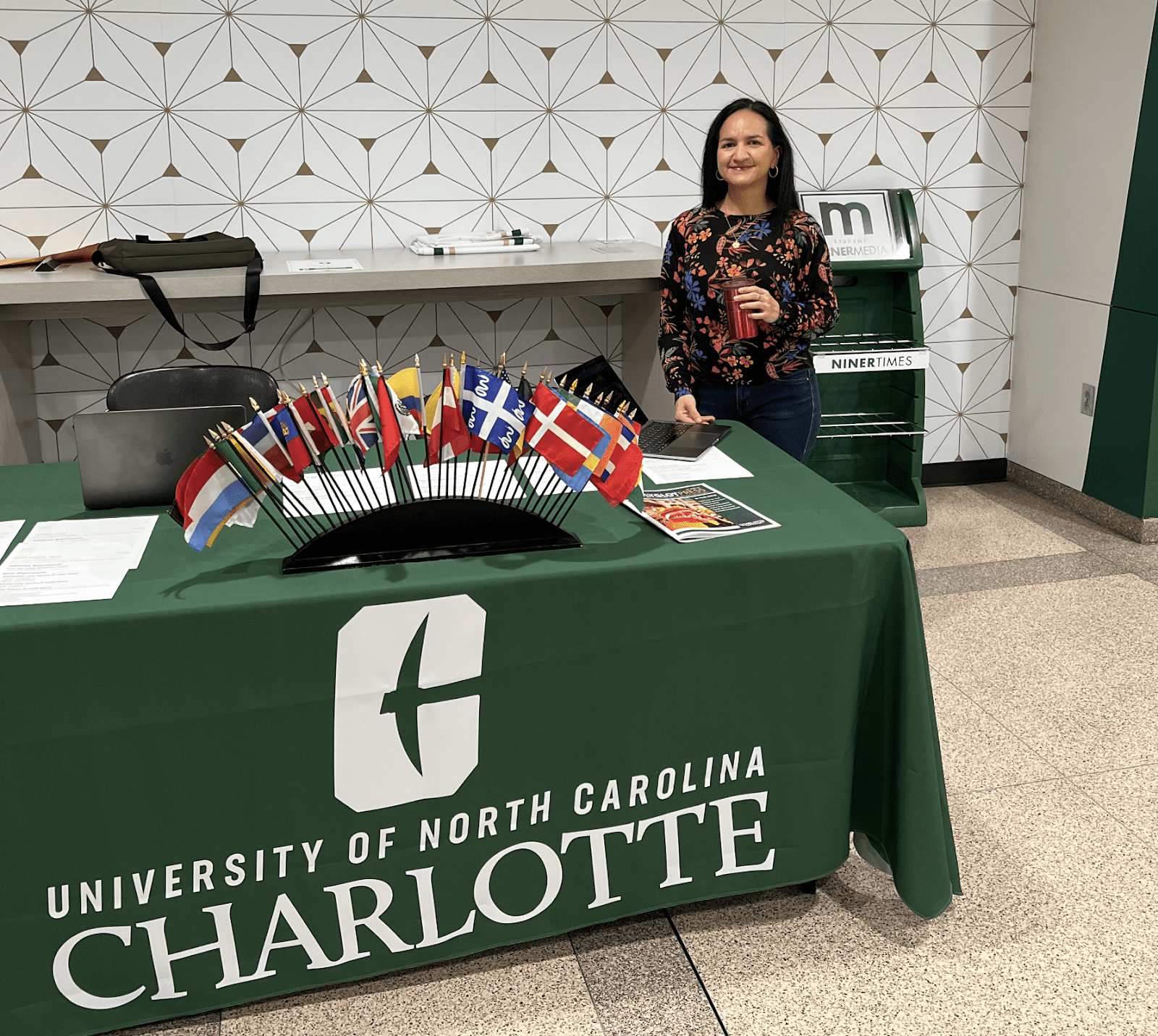 Photo of faculty member beside advertising table with small country flag decorations.